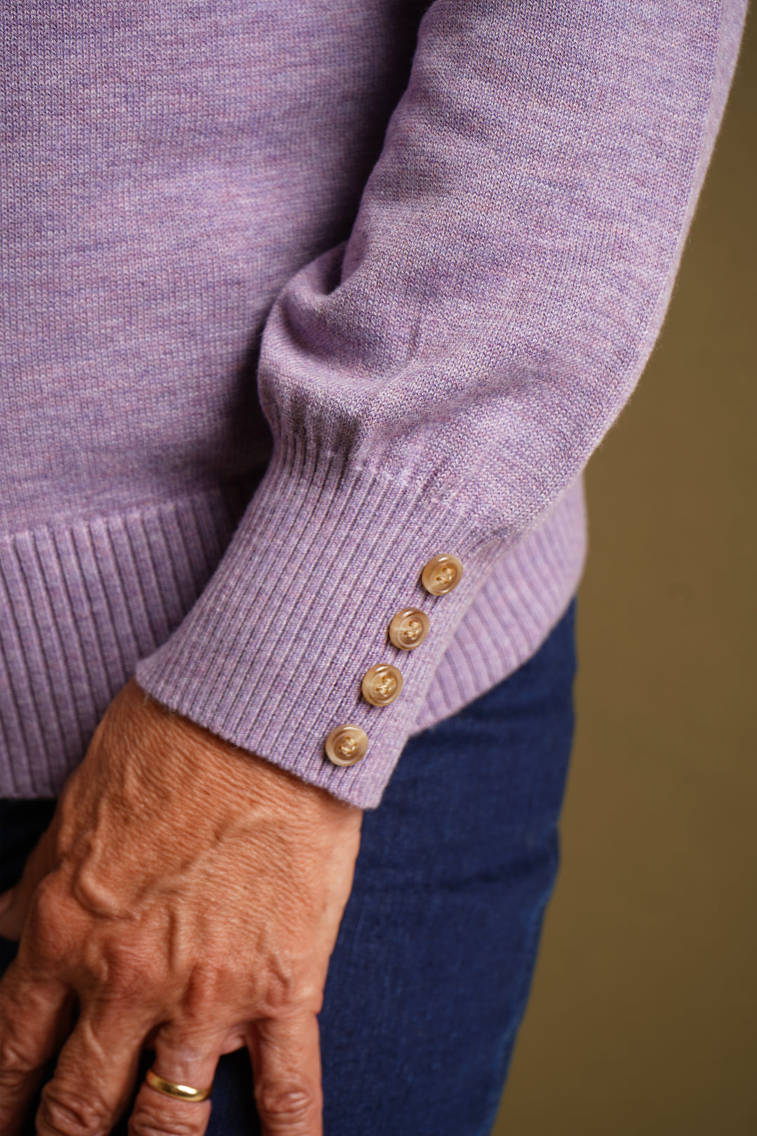 Close-up of a person wearing a lilac sweater with gold buttons on a blurred background