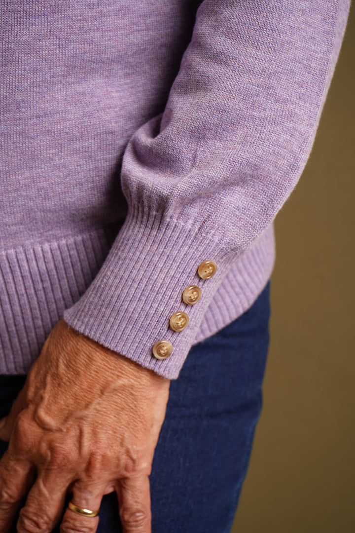 Close-up of a person wearing a lilac sweater with gold buttons on a blurred background