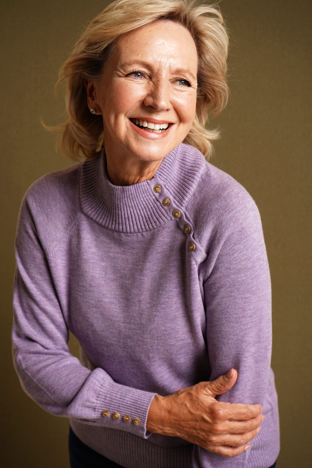 Woman wearing a lilac sweater with button details against a brown background
