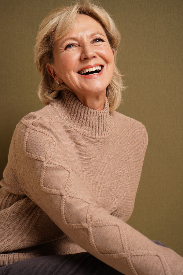 Woman wearing a oatmeal sweater against a brown background