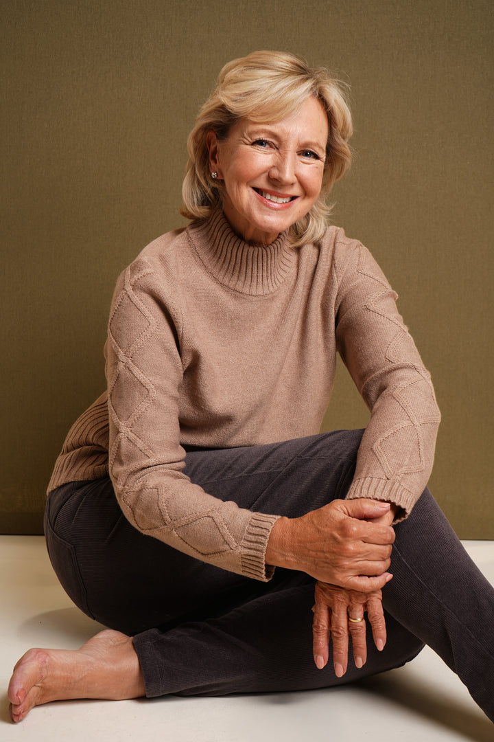 Woman wearing a oatmeal sweater sitting on a white surface with a brown background