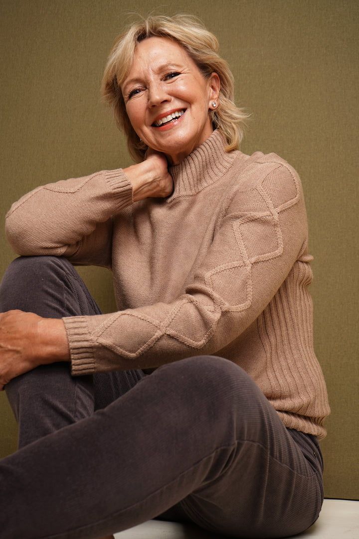 Woman wearing a oatmeal sweater sitting against a green background