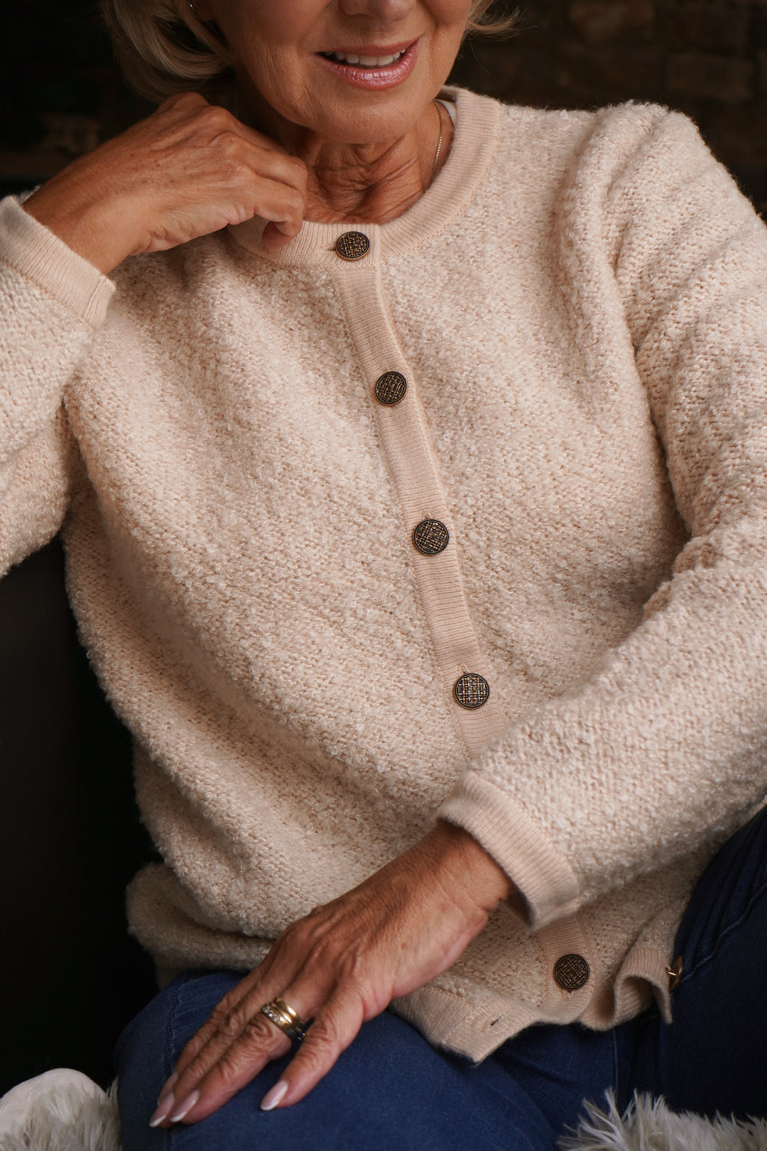 Close-up of a person wearing a beige cardigan with buttons, sitting on a dark surface.