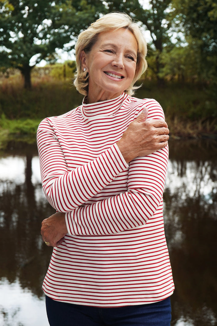 Woman in a red and white striped shirt standing by a body of water with trees in the background