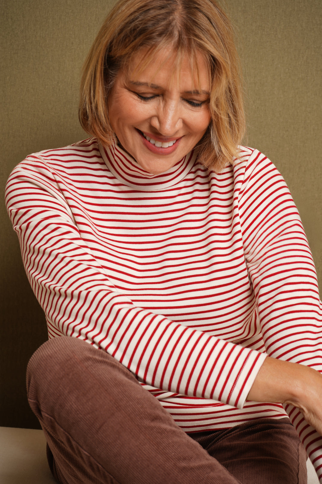 Woman wearing a red and white striped shirt sitting on a brown chair against a beige wall.