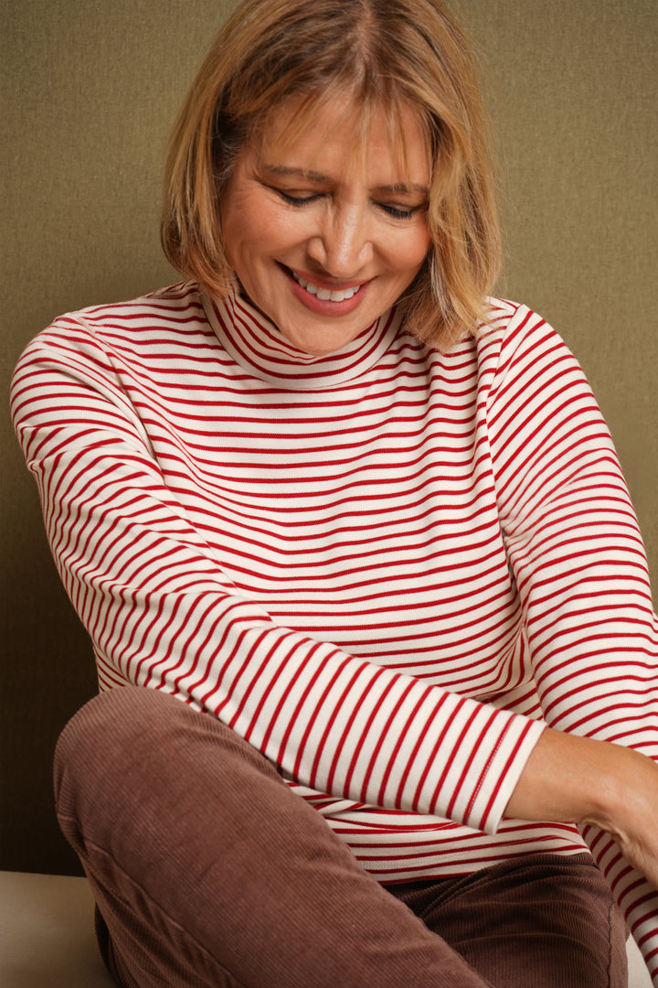Woman wearing a red and white striped shirt sitting on a brown chair against a beige wall.