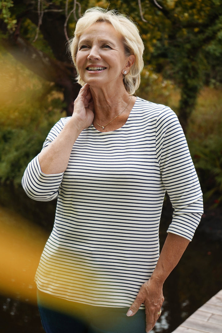 Woman wearing navy and white stripe top with 3/4 sleeves, outdoors with blurred background.