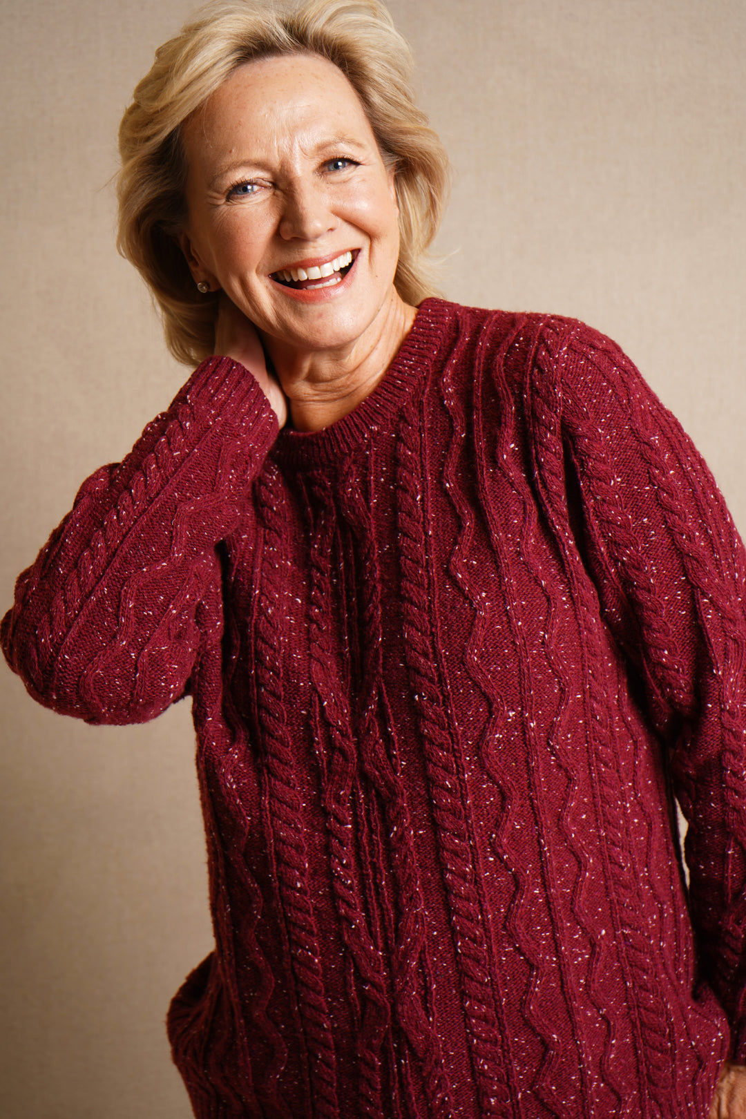 Woman wearing a claret cable knit sweater against a beige background