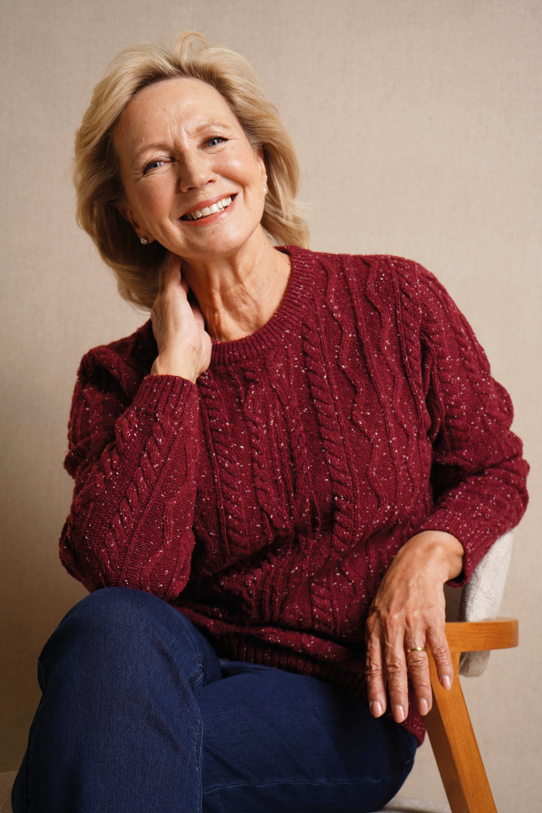 Woman wearing a red sweater sitting on a chair against a beige background