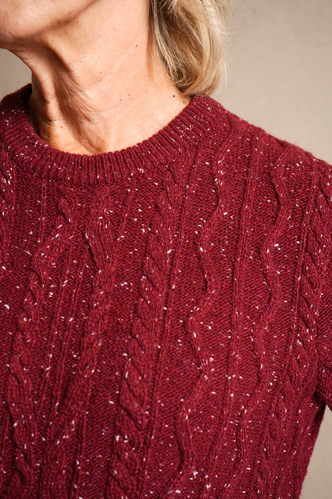 Close-up of a person wearing a red cable knit sweater against a neutral background