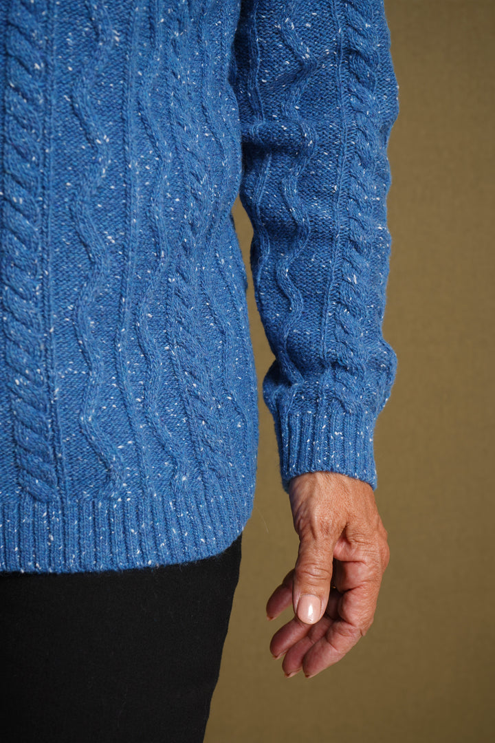 Blue cable knit sweater worn by a person on a brown background