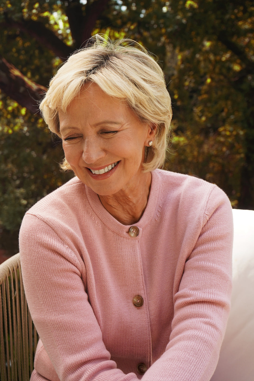 Woman wearing a pink sweater sitting outdoors with trees in the background