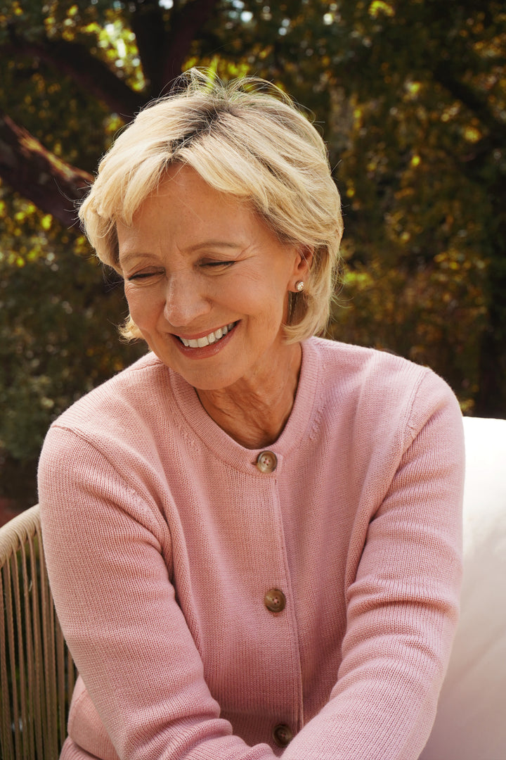 Woman wearing a pink sweater sitting outdoors with trees in the background