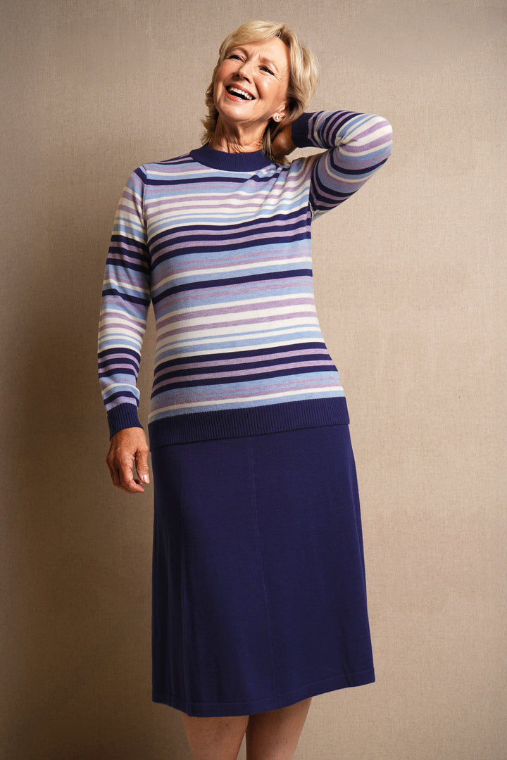Woman wearing a striped sweater and navy skirt against a beige background