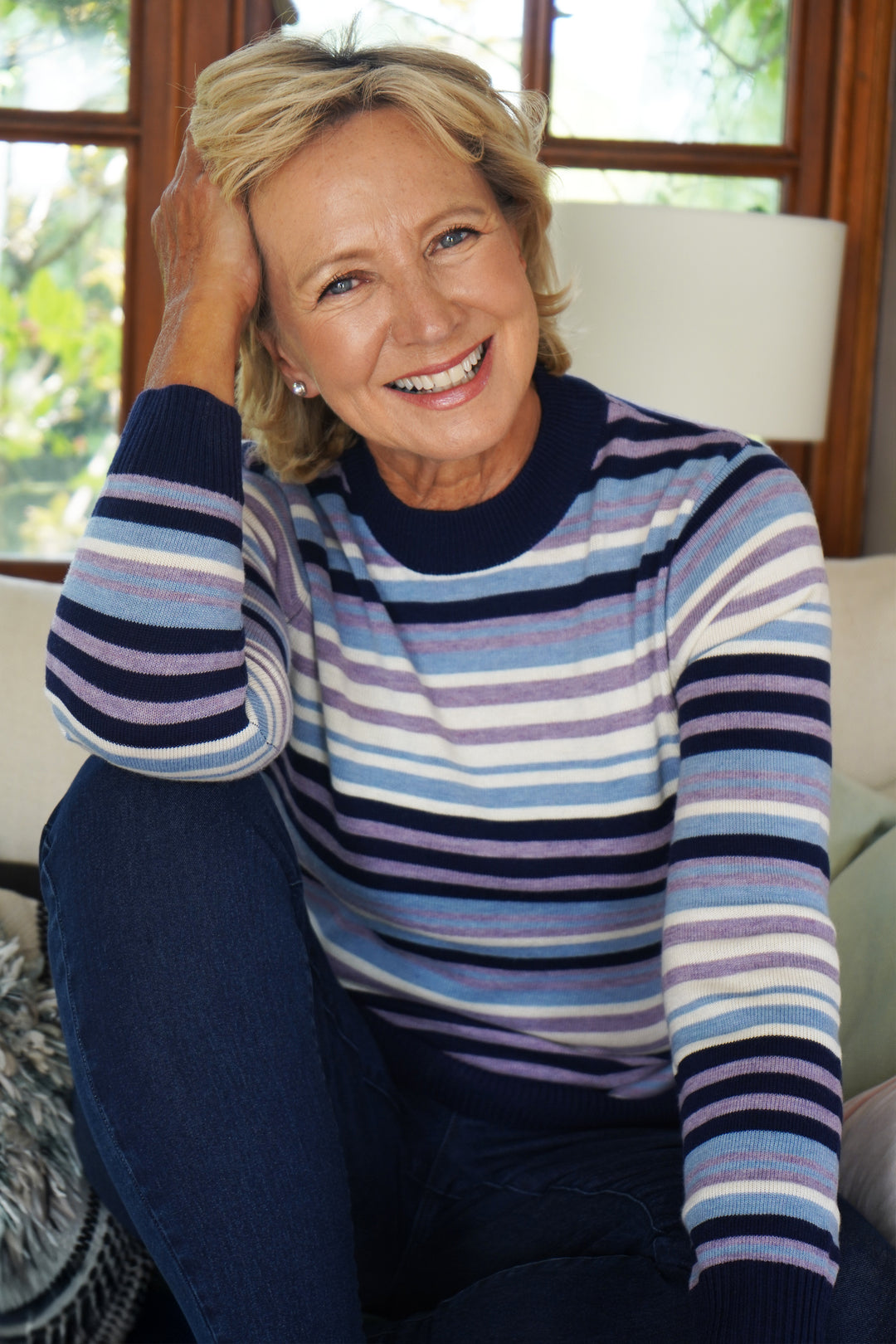 Woman wearing a striped sweater sitting in a room with a window in the background