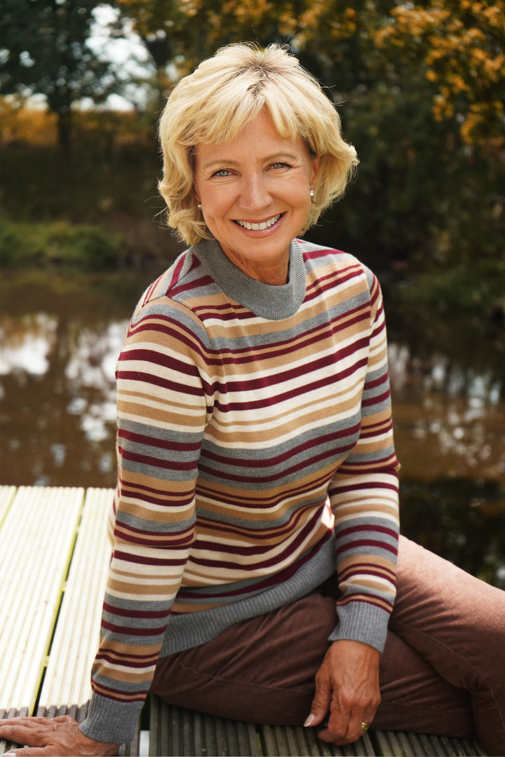 Woman wearing a striped sweater sitting by a body of water.