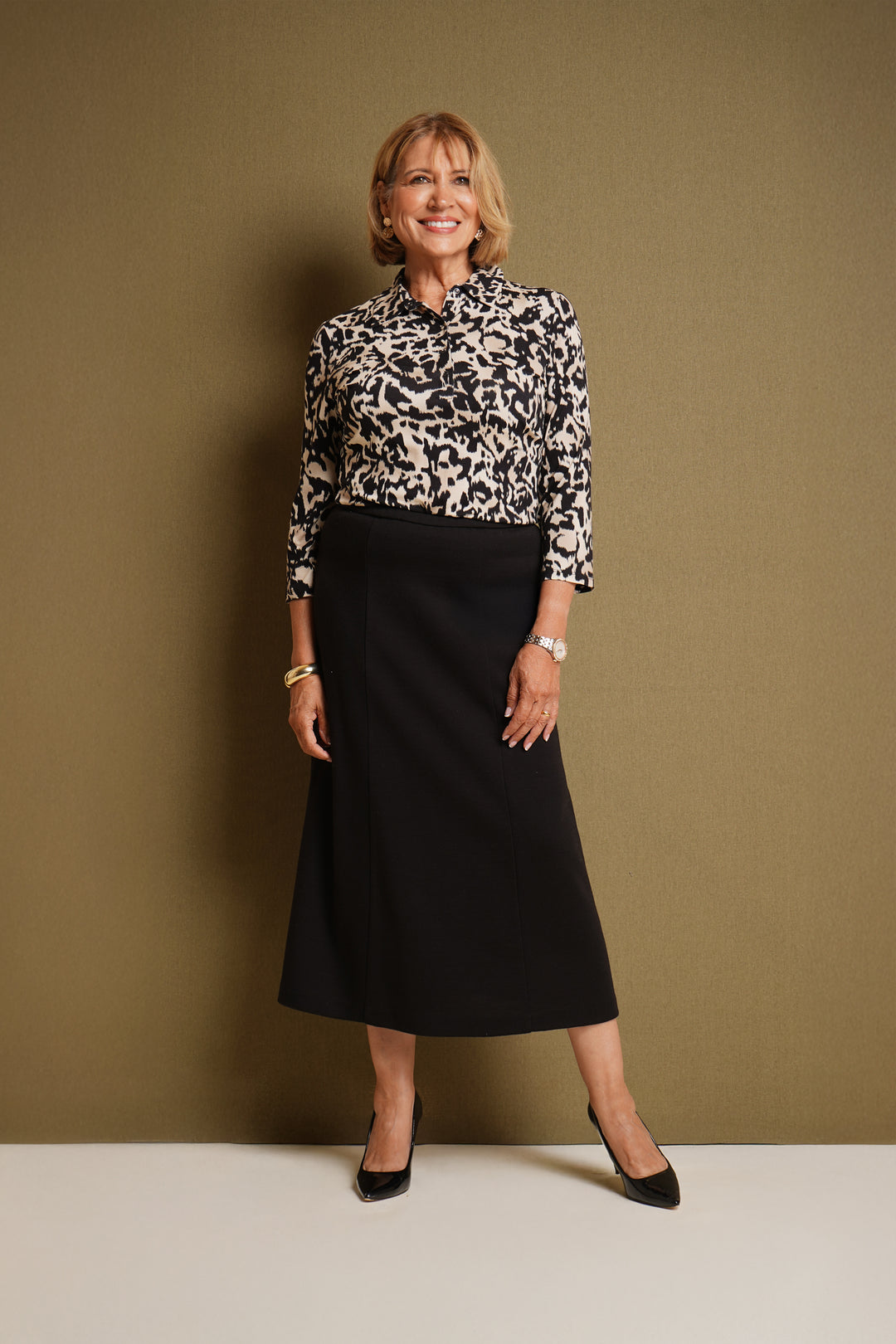 Woman is wearing an aminal print polo top with black skirt, against a brown background.