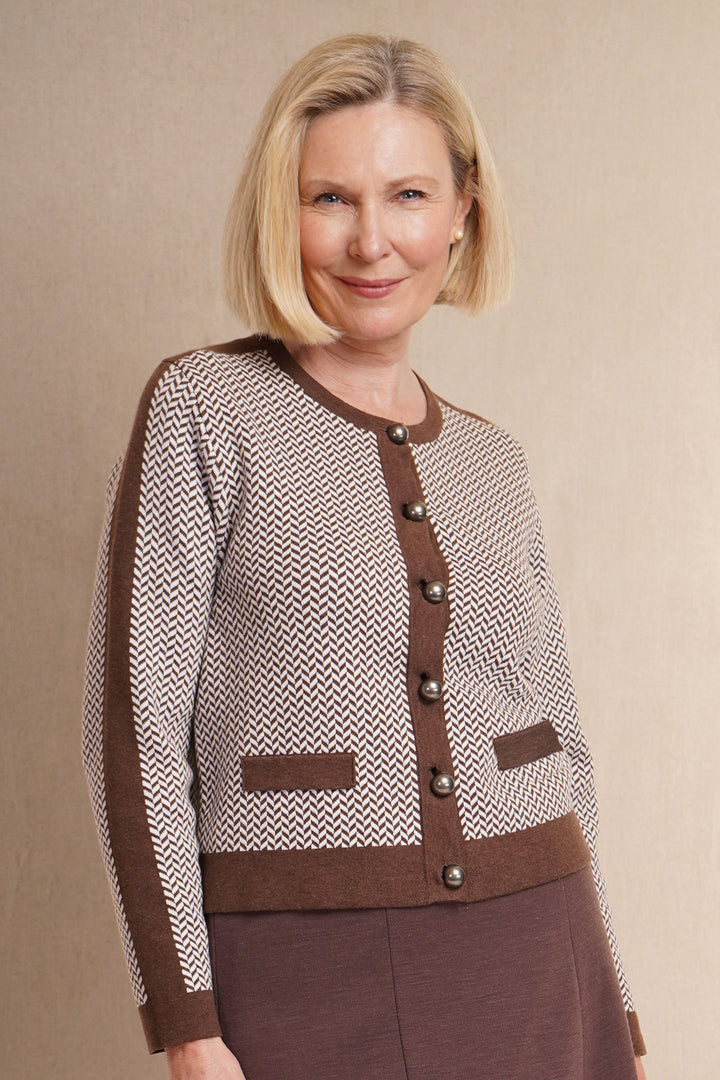 A woman wearing a  brown cardigan with a herringbone pattern, featuring large buttons and dark brown trim, with brown skirt.