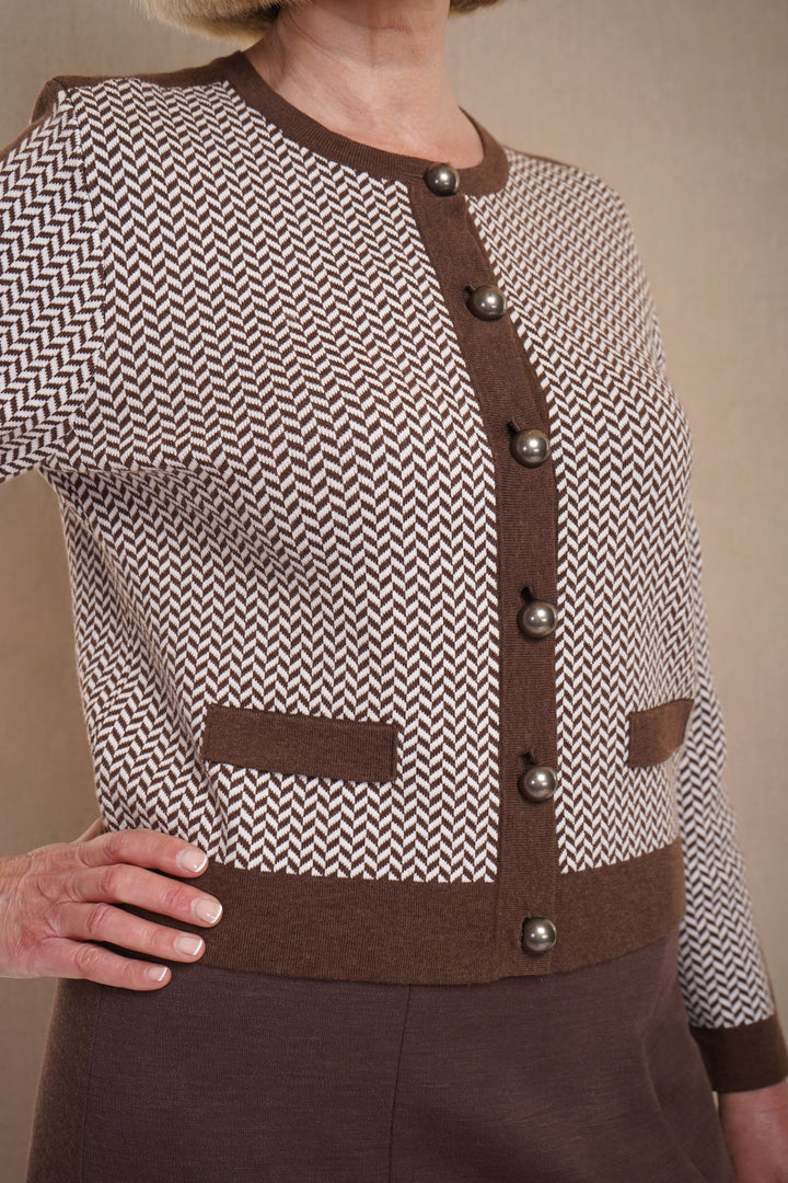 A woman wearing a  brown cardigan with a herringbone pattern, featuring large buttons and dark brown trim, with brown skirt.