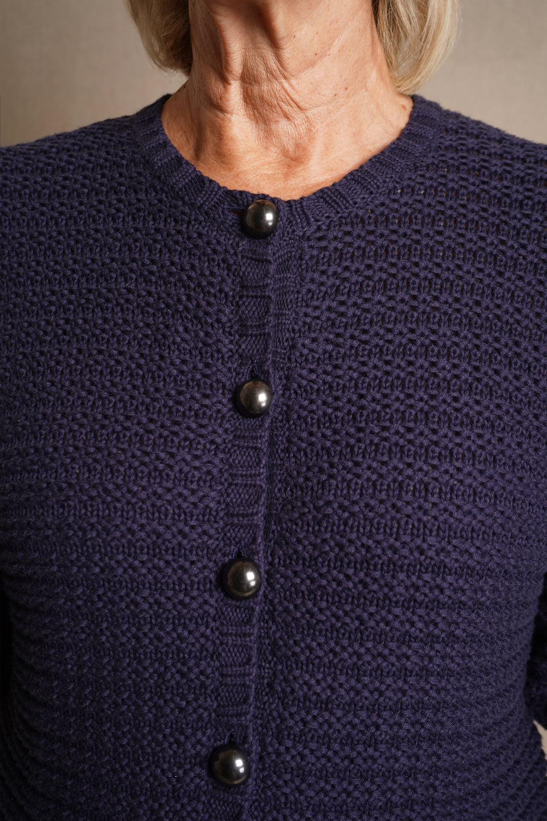 Navy textured cardigan with black buttons on a neutral background