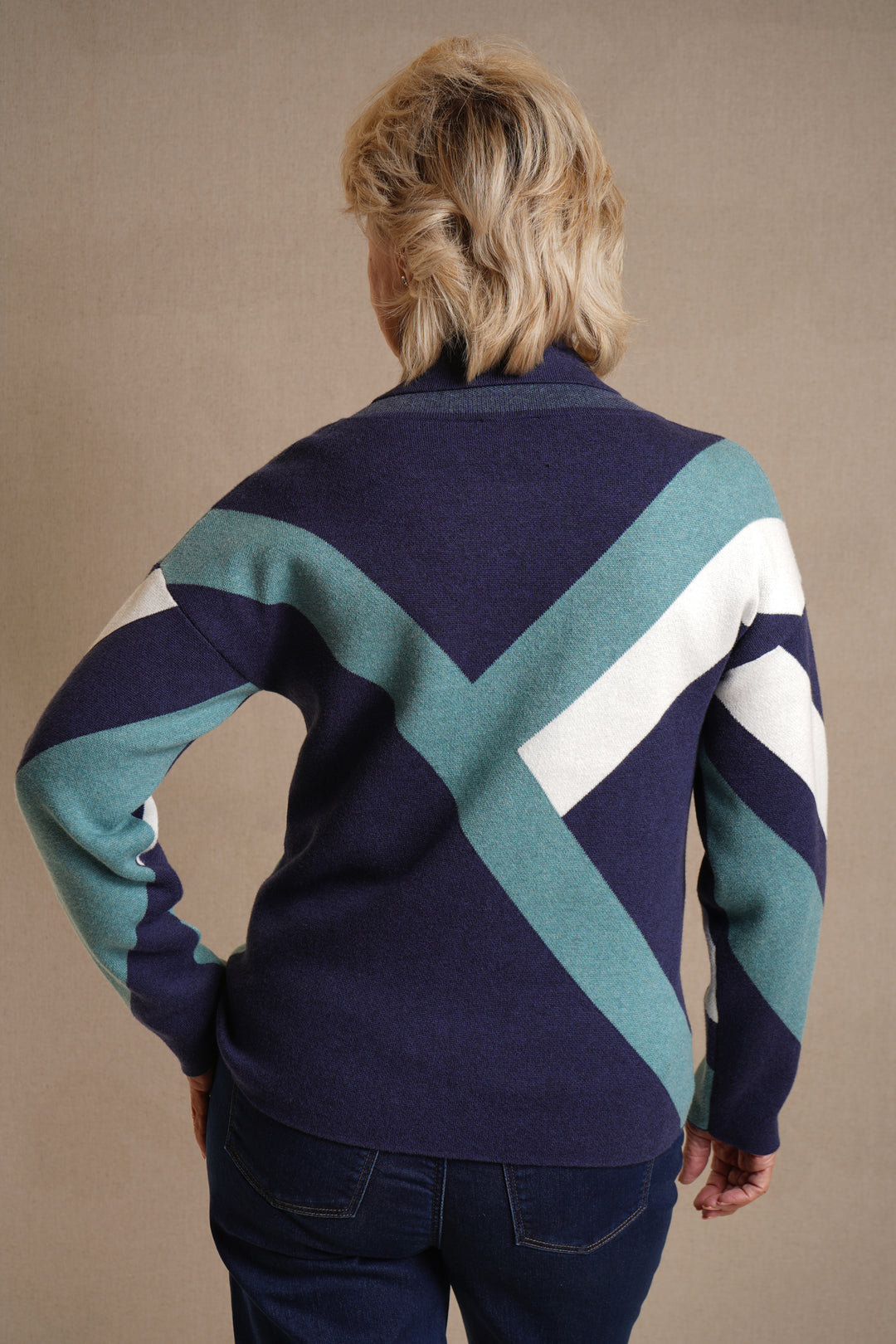 Person wearing a patterned sweater with blue, green, and white colors on a beige background