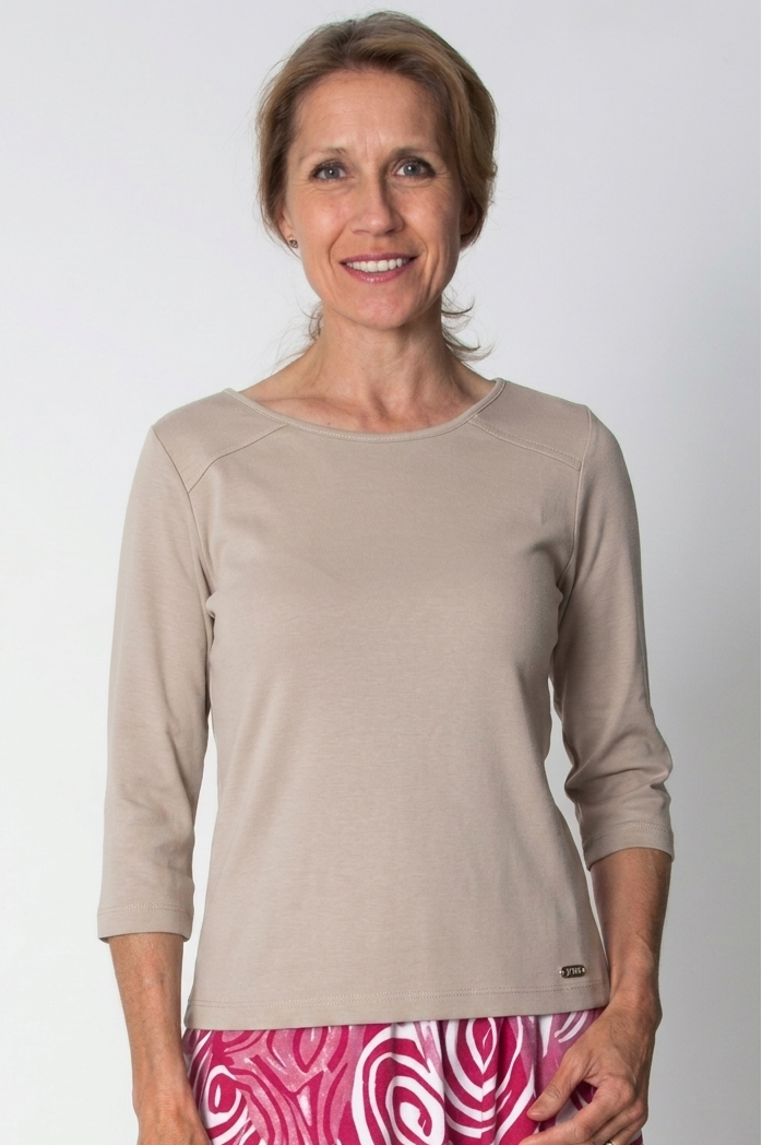 Woman wearing a beige long-sleeve top and pink patterned pants on a white background