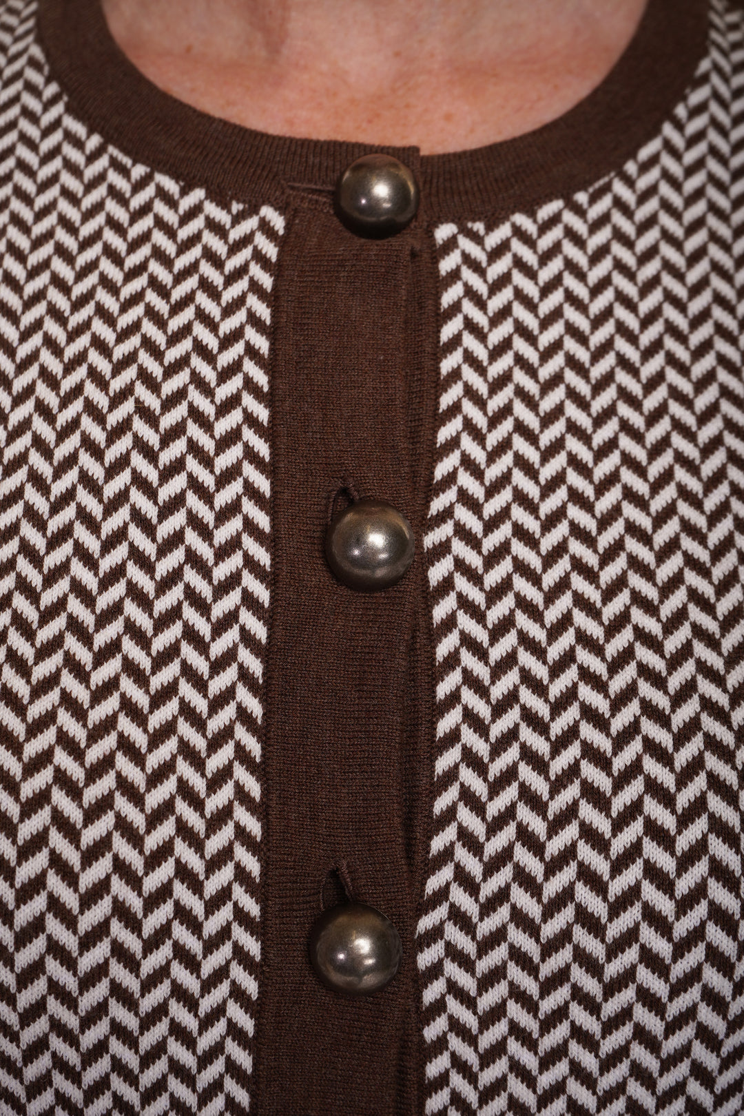 A close up of  brown cardigan with a herringbone pattern, featuring large buttons and dark brown trim.